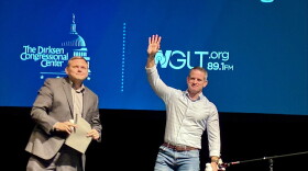 Two men stand on a stage with a WGLT and Dirksen Congressional Center logos int he background. 
