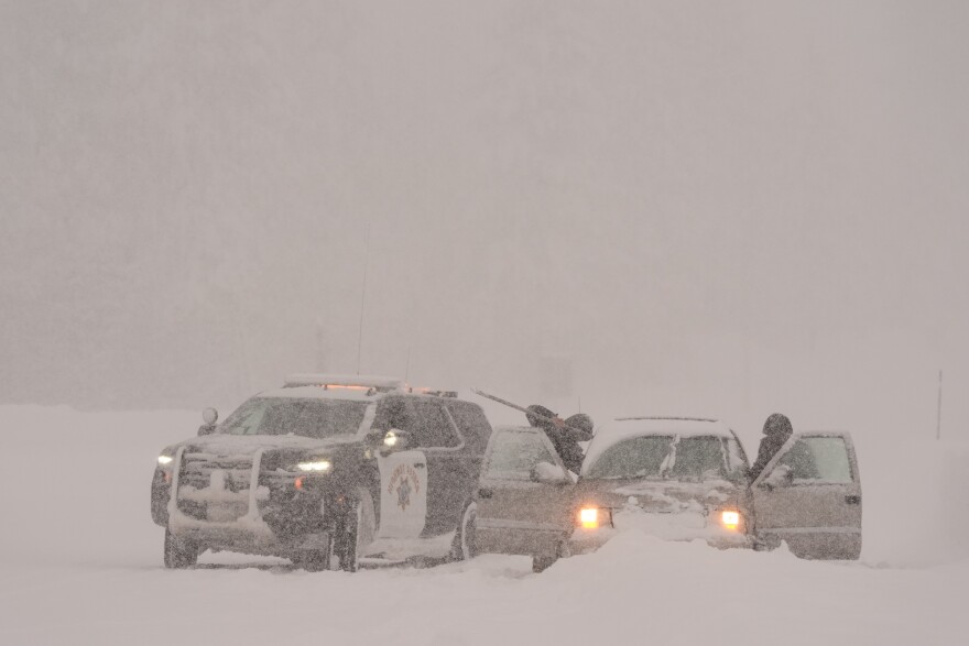A car is stuck in and covered with snow. A California Highway Patrol vehicle is parked next to it.