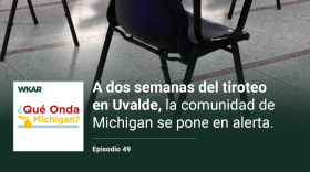 En la imagen se puede observar varias files de pupitres vacios en un aula. En el lado inferior de la imagen esta el logo de Que Onda Michigan sobre un fondo blanco. En la parte derecha las siguientes palabras estan escritas: "A dos semanas del tiroteo en Uvalde, la comunidad de Michigan se pone en alerta"  y "Episodio 49". 