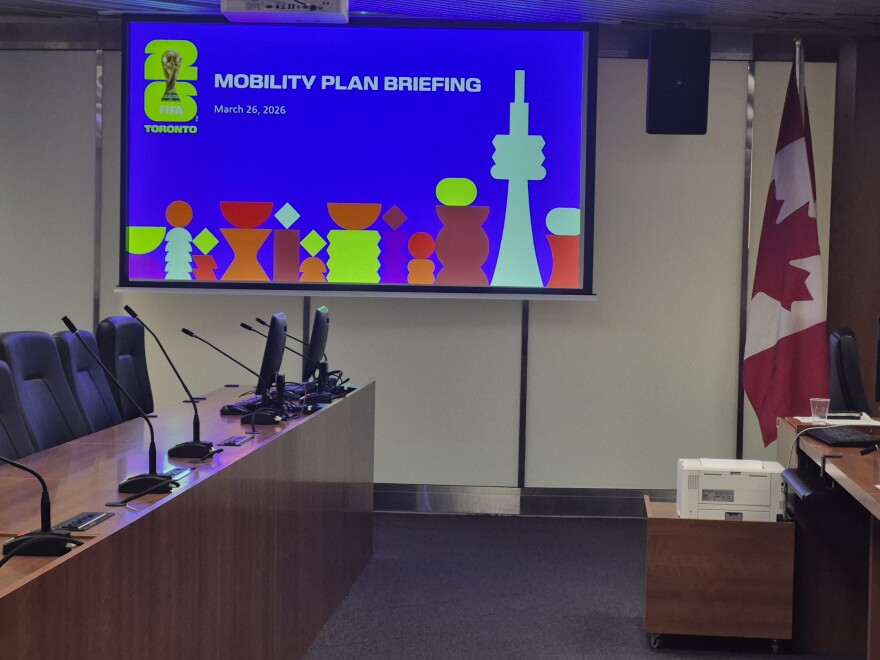 Inside FIFA Mobility Plan Briefing at Toronto City Hall where a screen displays the event details and FIFA logo. Canadian flag is present to the right of screen display. 