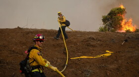 Cal Fire firefighters carry a fire hose up a hillside during the Sandy Fire in Simi Valley on May 18, 2026.