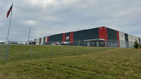 Photograph of L&M Fleet Supply distribution center with building, yard, fence, cars, and an American flag