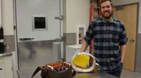 Warren Hansen stands beside a white radio collar used to track moose. (Photo by Elizabeth Jenkins/Alaska’s Energy Desk)