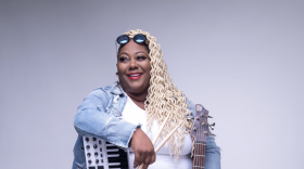 musician Lacretia Bolden sits with a keyboard, drumsticks and guitar while smiling and looking off to the right