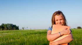 A young girl smiling and holding books in a field