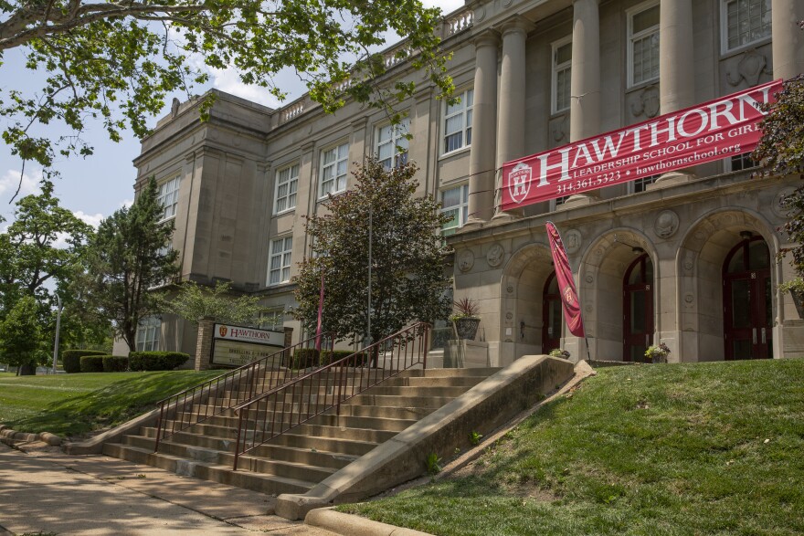 The exterior of a large stone building. Above its door is a red banner reading "Hawthorn Leadership School for Girls."