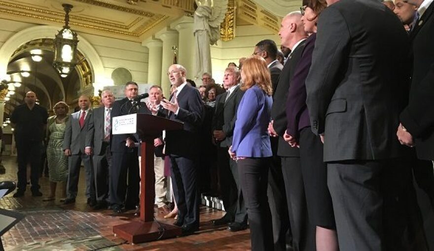 Wolf flanked by state, county, and municipal officials who support his Restore PA proposal, urges other lawmakers to get on board. (Katie Meyer/WITF)