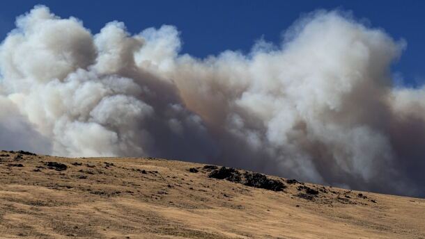 A hilly terrain with smoke filling an otherwise blue sky.