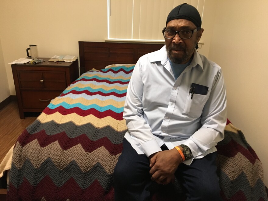 Timothy Lewis, a resident of the Oaks at 14th, sits on his bed that's covered with an afghan blanket he crocheted.