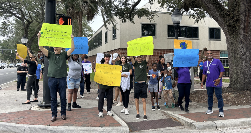 St. Francis staff, volunteers and people experiencingg homelessness hold up signs during their walk through downtown Gainesville during St. Francis House’s World Homeless Day event on Oct. 10, 2025. (Victoria Riccobono/WUFT News)