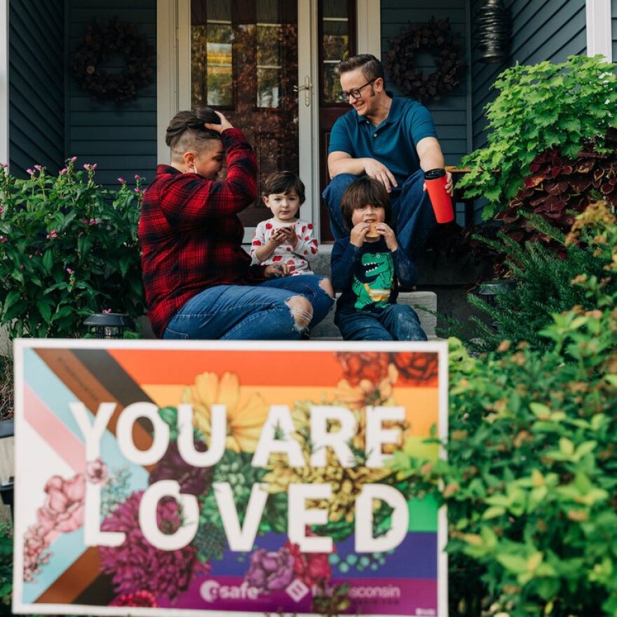 Rae Senarighi (top right) sits on the with his family behind a "You Are Loved" yard sign, based off the design he created for the billboard campaign.