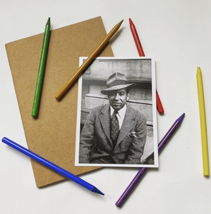 Photo postcard of poet Langston Hughes in 1939, taken by Carl Van Vehten, next to a sketchbook and surrounded by woodless colored pencils. 