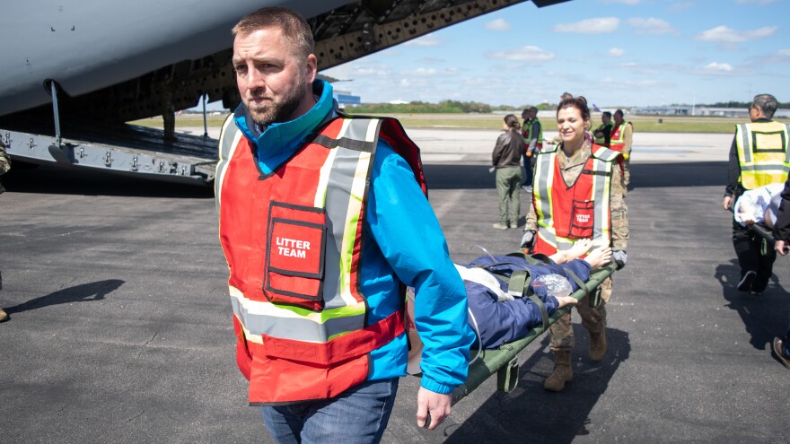 Two men carry a mannequin on a stretcher off a cargo airplane