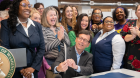 Governor Bob Ferguson points to an executive order as a group of women cheer and applaud.