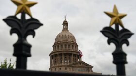 The top of the Texas State Capitol building is seen through the wrought iron fence that surrounds the property.