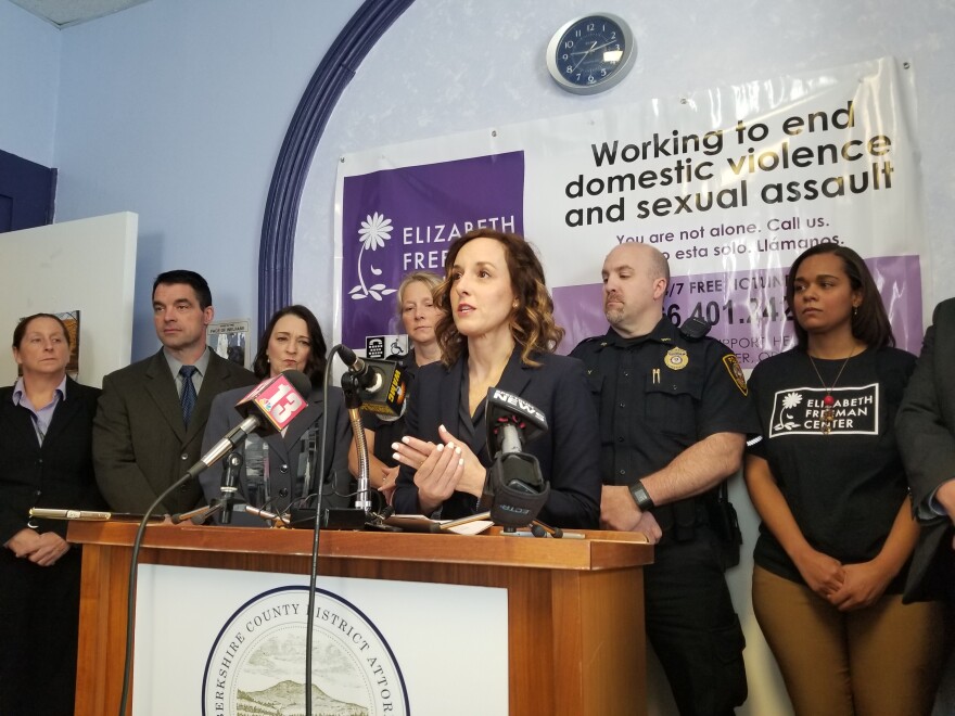 Andrea Harrington stands at a podium with a row of people behind her.