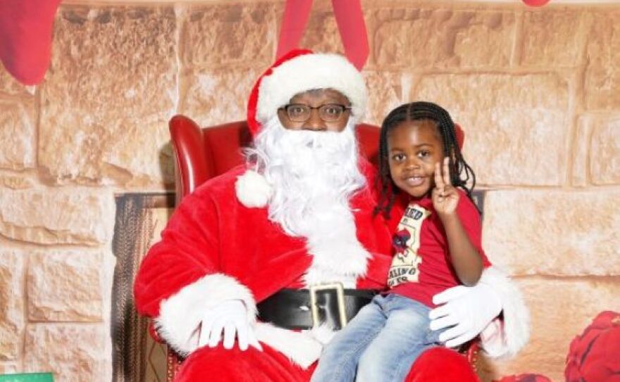 little sits on Santa's lap showing a peace sign