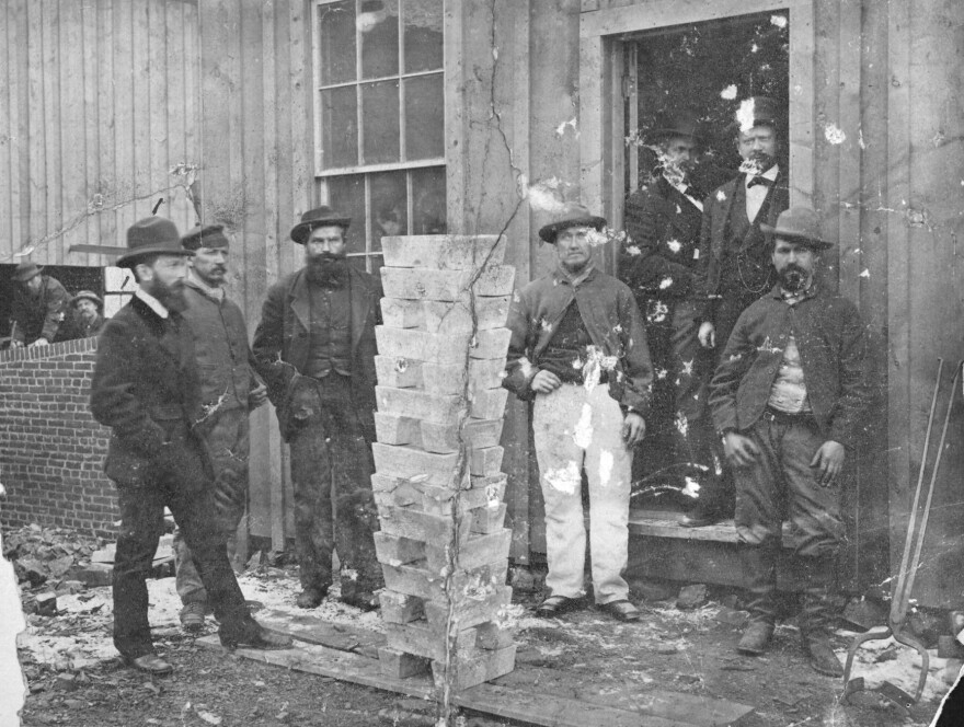 Workers at the Boston & Colorado Gold and Silver Smelting Company pose next to stacked silver ingots in Empire in this 1875 photograph.
