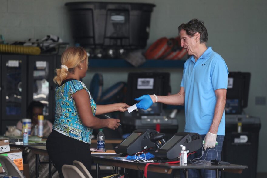 A poll worker in Miami Beach checks in George Hanley, who is wearing protective gloves, as he prepares to cast a ballot during the Florida presidential primary as the coronavirus pandemic continues.