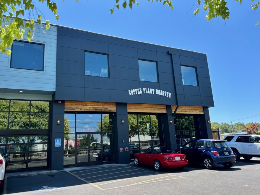 The front of a coffee shop, with cars parked outside bays of large windows. 
