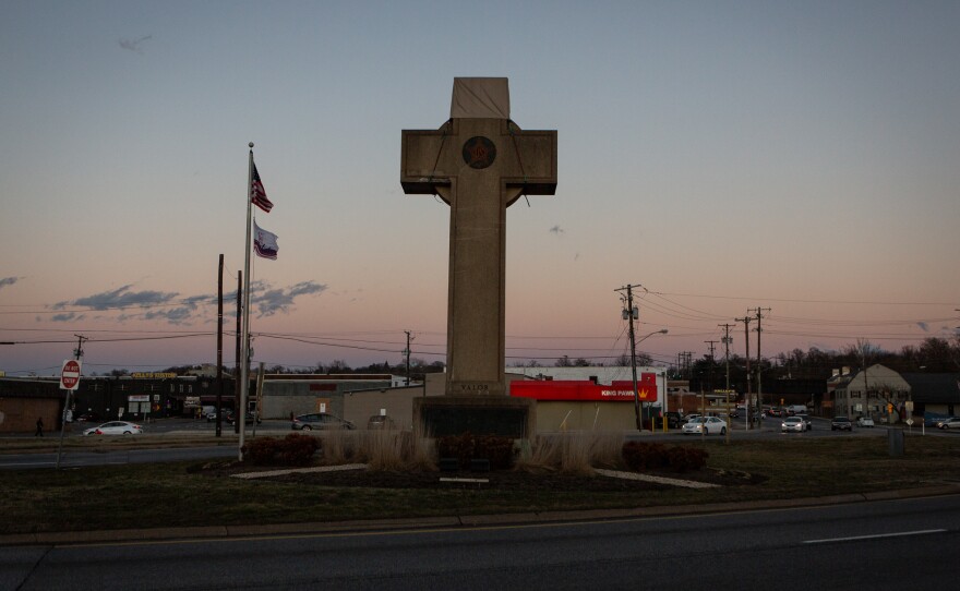 The cross sits in the median at a busy five-way intersection.