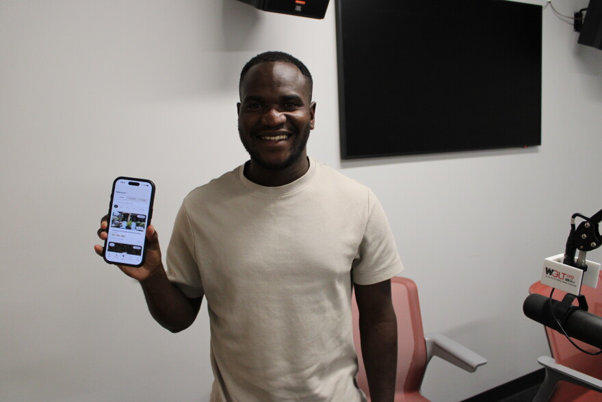 A man holds up his phone to show an app he created, and smiles. 
