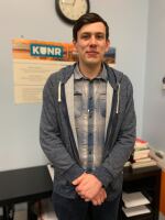 Jayden Perez is standing in the KUNR newsroom. He is looking toward the camera and smiling.