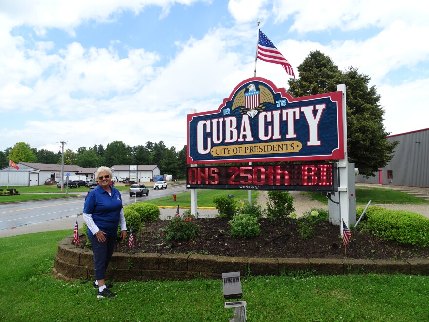 Woman stands in front of Cuba City, "City of Presidents" sign outdoors. 
