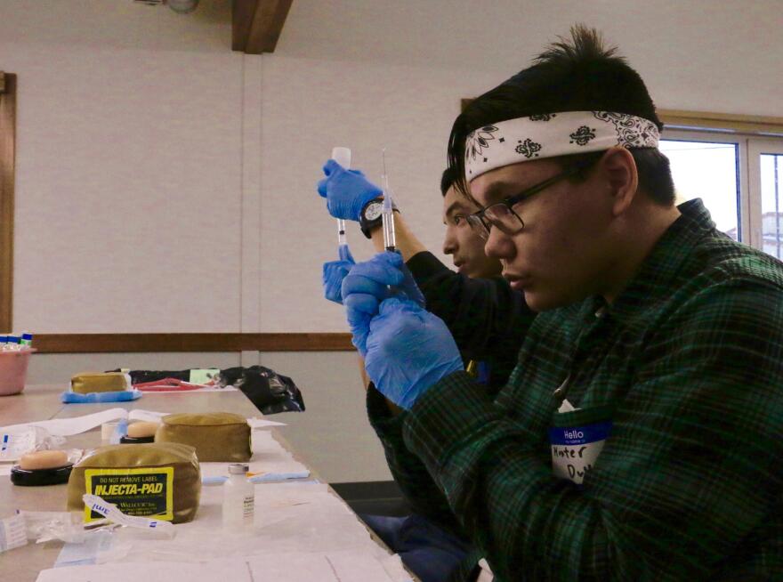 Bethel Regional High School junior Hunter Dull (front) and senior Matthew Hunter (back) fill syringes with 2.5 mL of saline solution at the RRANN camp at Yuut Elitnaurviat on December 2, 2017. (Anna Rose MacArthur / KYUK)