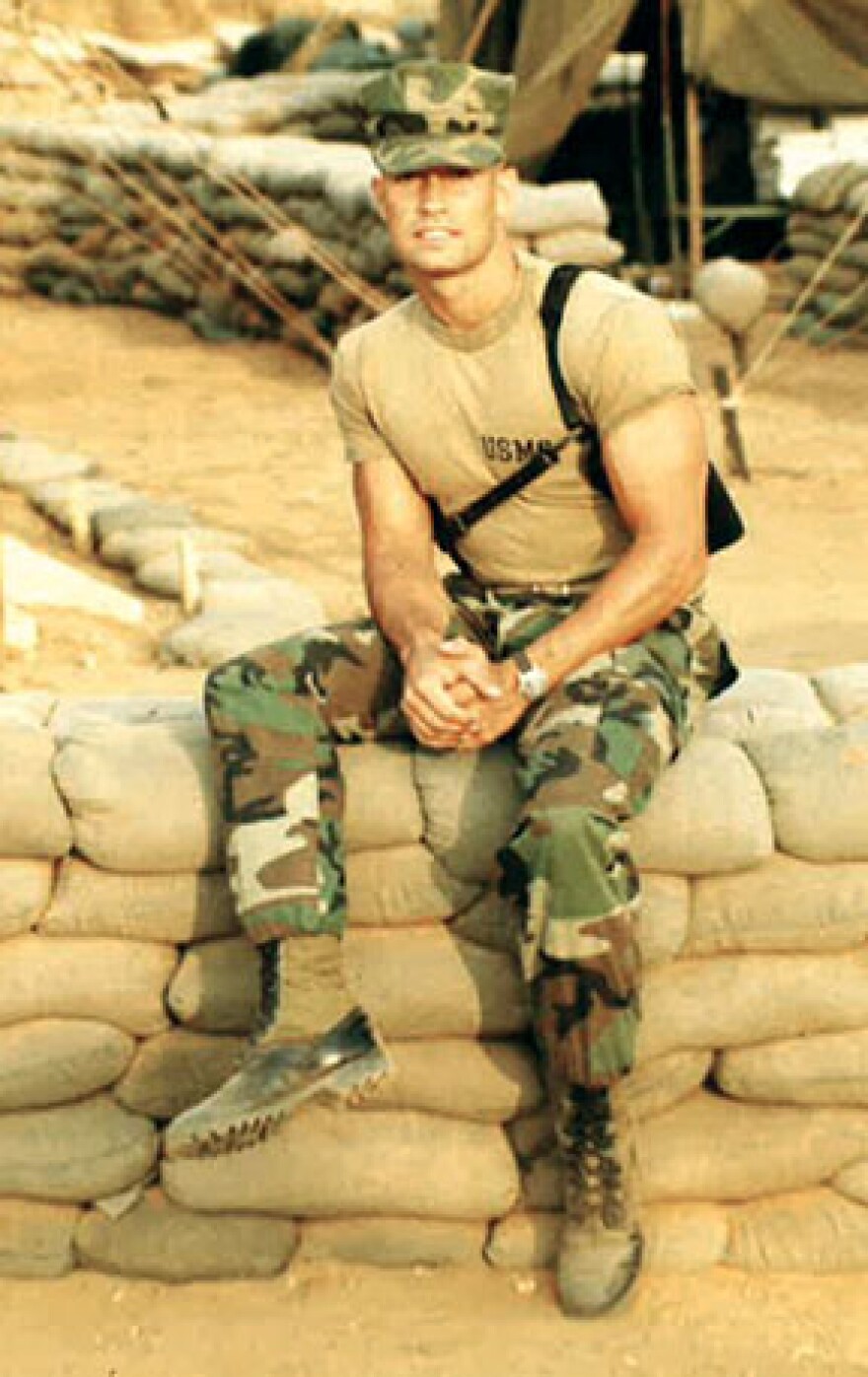 Miles Burdine in 1983 in military fatigues sits on sandbag wall