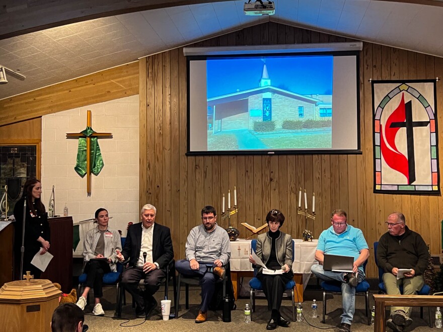 People sit on chairs on a church stage.