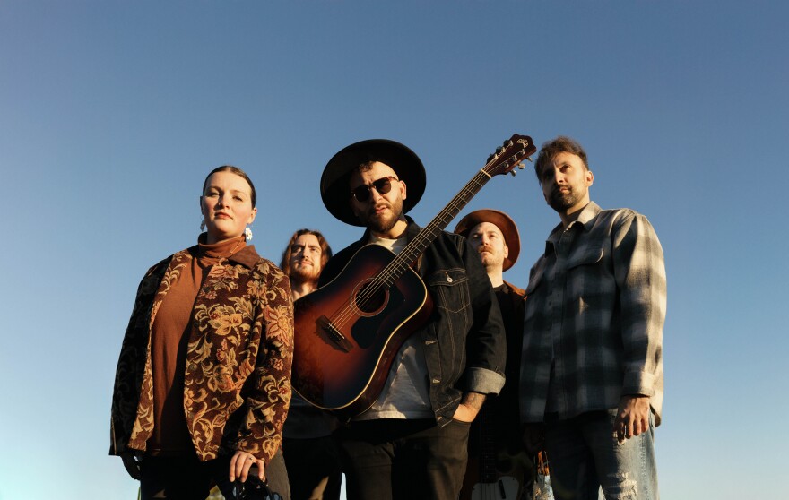 Photo of VOYAGR, with the man in the middle wearing a guitar around his body