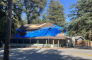 A dilapidated building is covered in a large blue tarp and its windows are all boarded up.