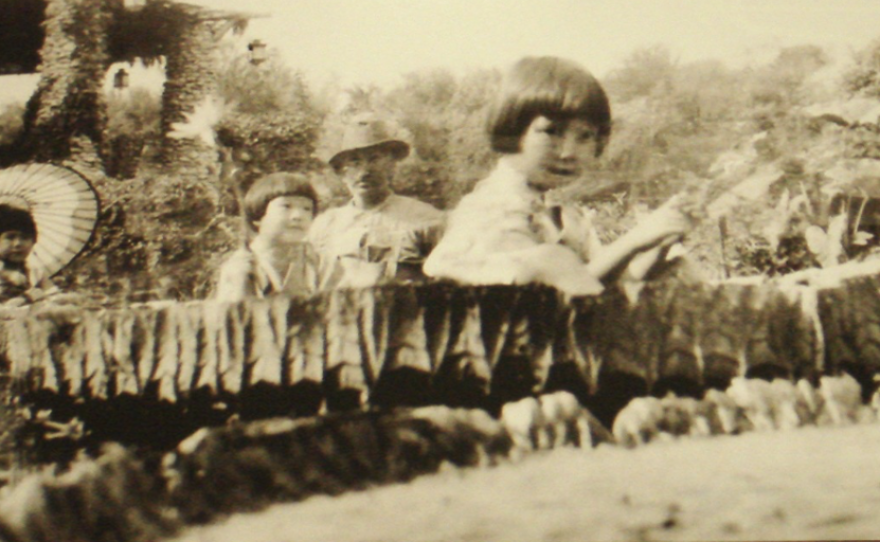 A picture taken in the 1920s of girls sitting in a giant water lily. Gardener Hugo Gerhardt is in the background.