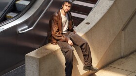 The artist Alex G sits on a concrete railing next to a staircase and escalator.