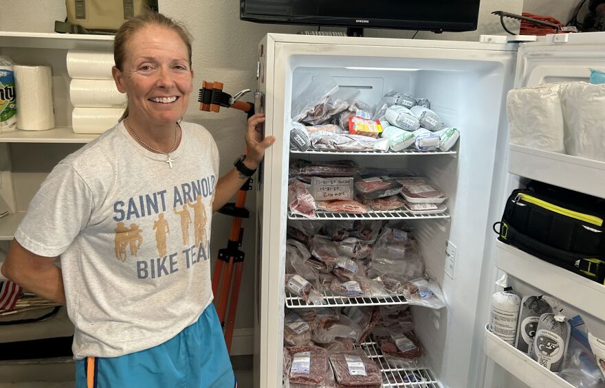 Kasey Guentert stands next to a white stand-up freezer in her garage. The freezer has multiple rows, all of which are filled with vacuum-sealed cuts of beef.
