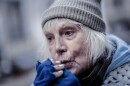 An older woman with white hair, a knit cap and fingerless mittens