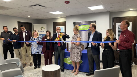 A man holding a large pair of ceremonial scissors cuts a ribbon held by multiple people to open a new building. 