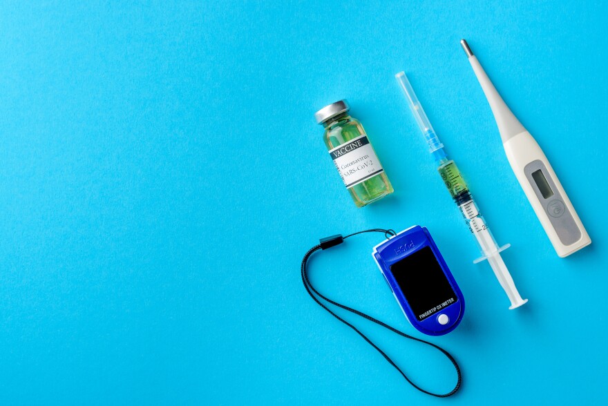 Top view of medical accessories for diagnosis and treatment of coronavirus, pulse oximeter, vaccine with syringe and thermometer, blue background, flat lay