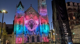 Colored lights cover the facade of a church at dusk.