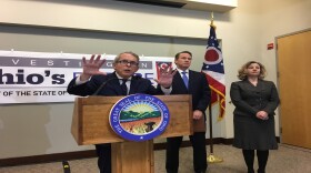 Gov. Mike DeWine gestures at his budget unveiling, as Lt. Gov. Jon Husted and budget director Kimberly Murnieks stand nearby.