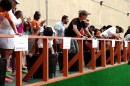 Teams of people standing on platform behind multiple competitors stomping on grapes in a barrel