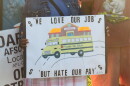 Close-up of a Princeton bus driver holding a sign that reads "We love our job, but hate our pay."