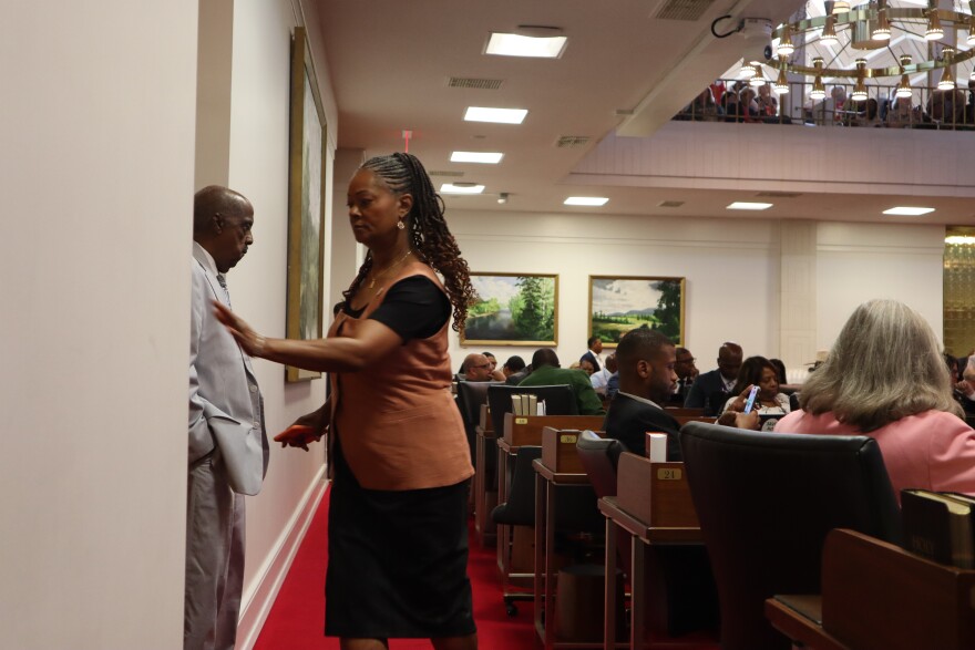 Carla Cunningham, wearing an orange vest over a black dress, holds her hand to open a door and exit the North Carolina House after crossing party lines to override the governor's veto of an immigration bill on Tuesday, July 29, 2025.
