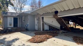 An abandoned home. It's grey with beige bricks and white trim. The garage to the right is destroyed.