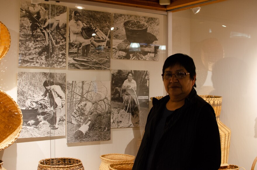 Faye Junaluska stands in front of pictures of her mother at the Qualla Arts & Crafts Cooperative. 