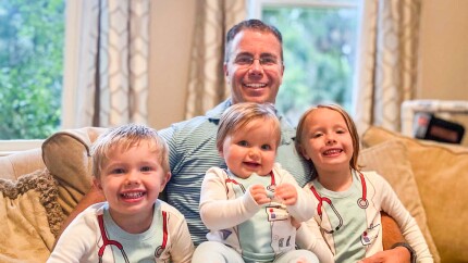 Nicholas Steinour sits on a couch with his three children on his lap.