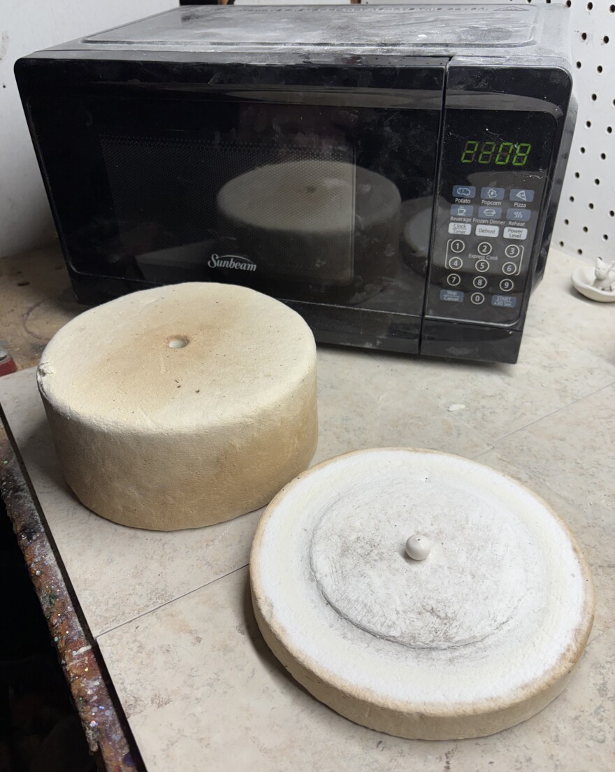 an off-white round base with next to a cylinder in front of a microwave.