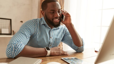 Happy afro american businessman in shirt talking by phone with client and smiling while working at his working place at home. Freelance. Home office