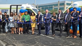 A group of people in dress clothes cut a ribbon in front of two transit vans